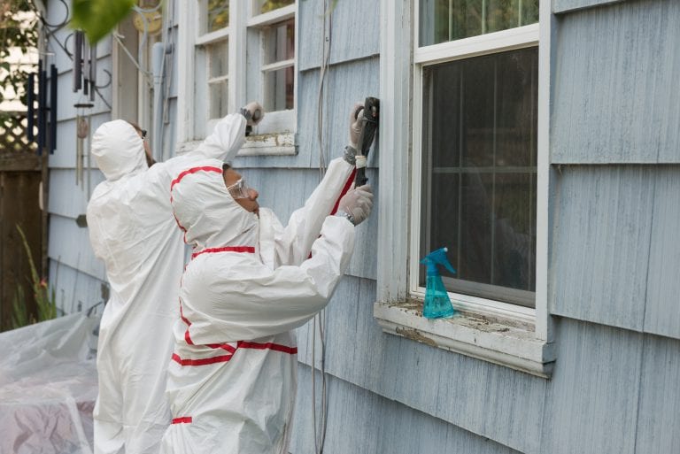 Two house painters in hazmat suits removing lead paint from an old house.